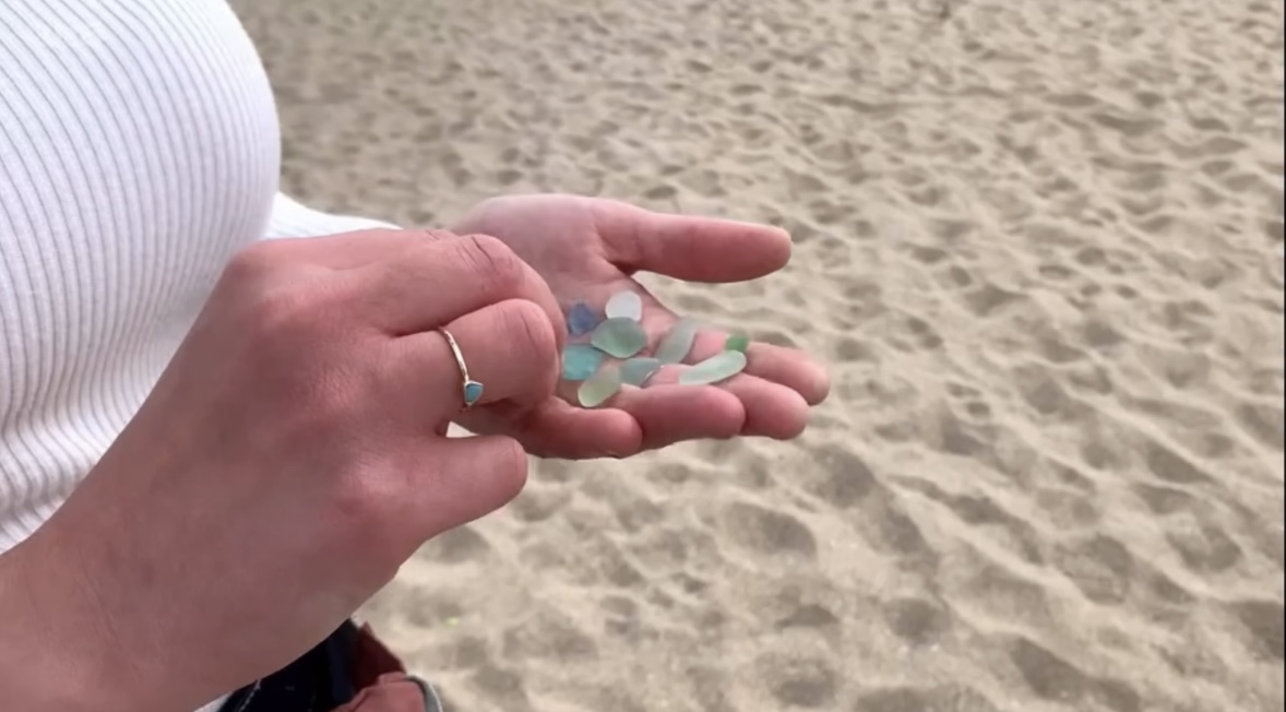 Sadie Jewellery designer holding sea glass over sand at Holywell Bay Cornwall during Escape to the Country filming