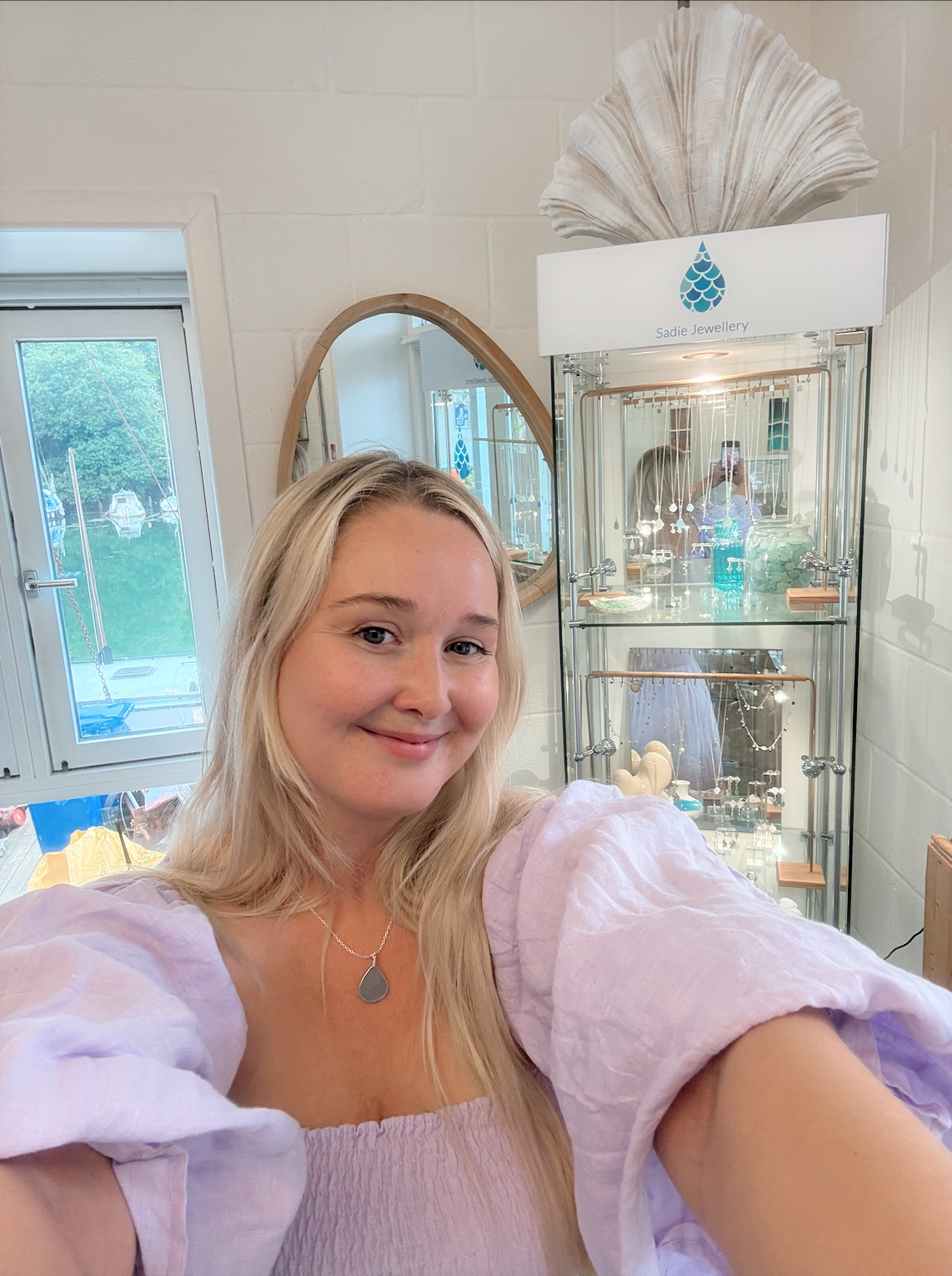 Sadie in her studio with sea glass jewellery displayed in the background, showcasing the handcrafted designs of Sadie Jewellery